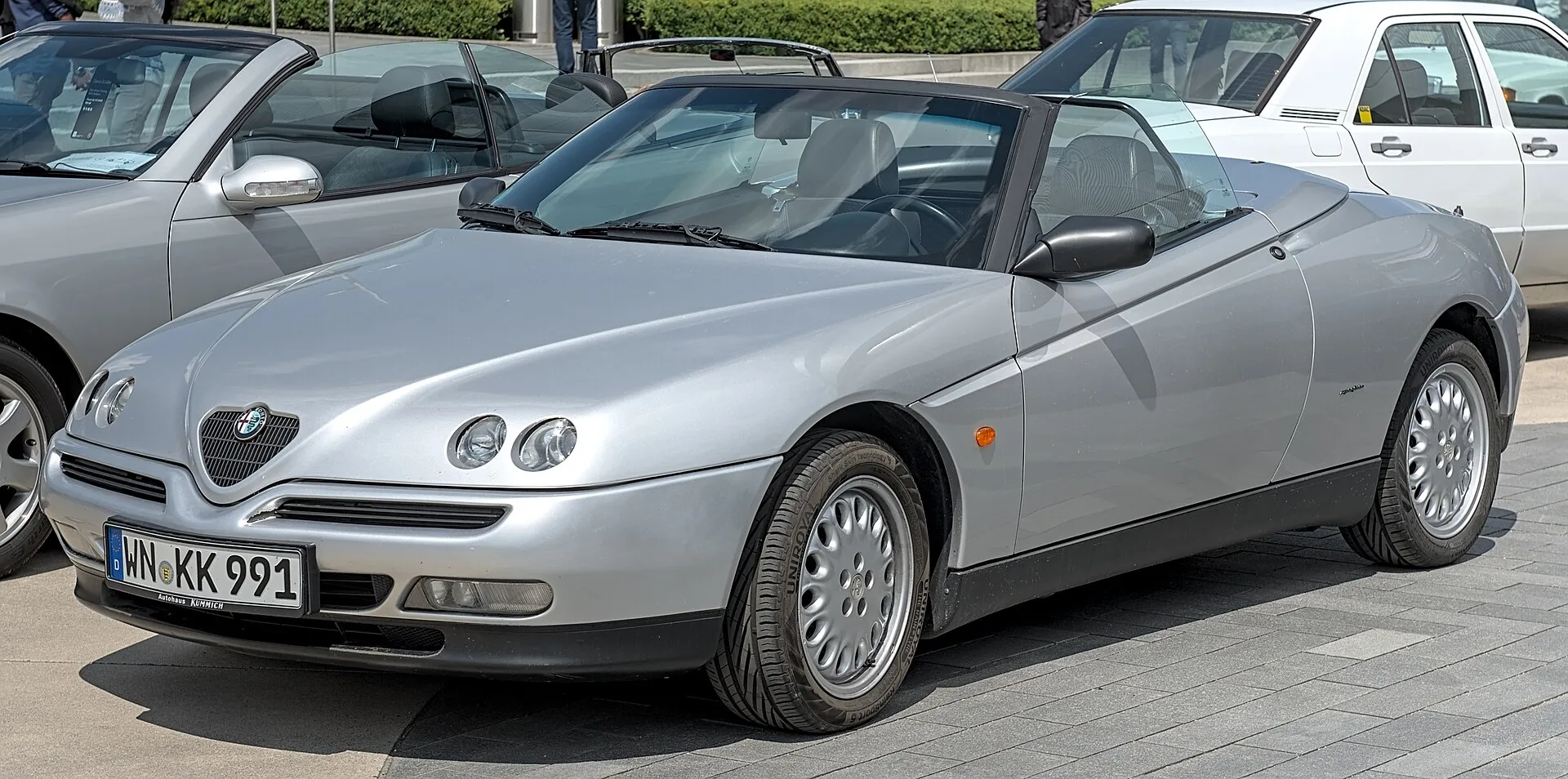 A silver 1990s Alfa Romeo Spider with its roof down